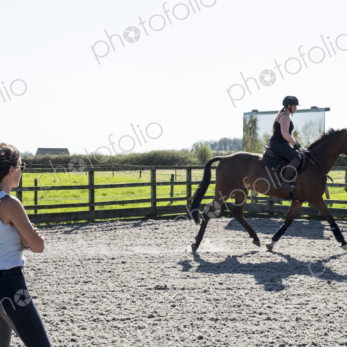 Woman, a horse trainer watching a young woman riding on a brown bay horse in a…
