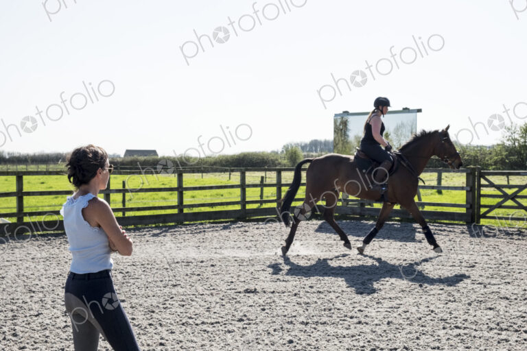 Woman, a horse trainer watching a young woman riding on a brown bay horse in a…