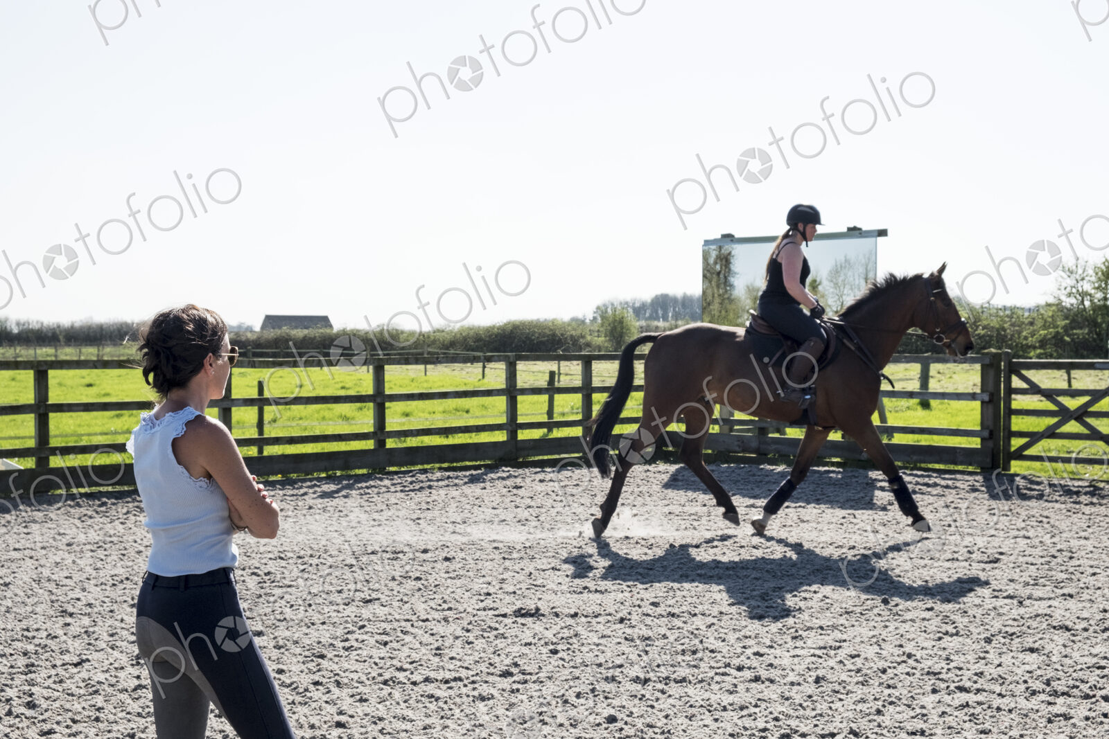 Woman, a horse trainer watching a young woman riding on a brown bay horse in a…