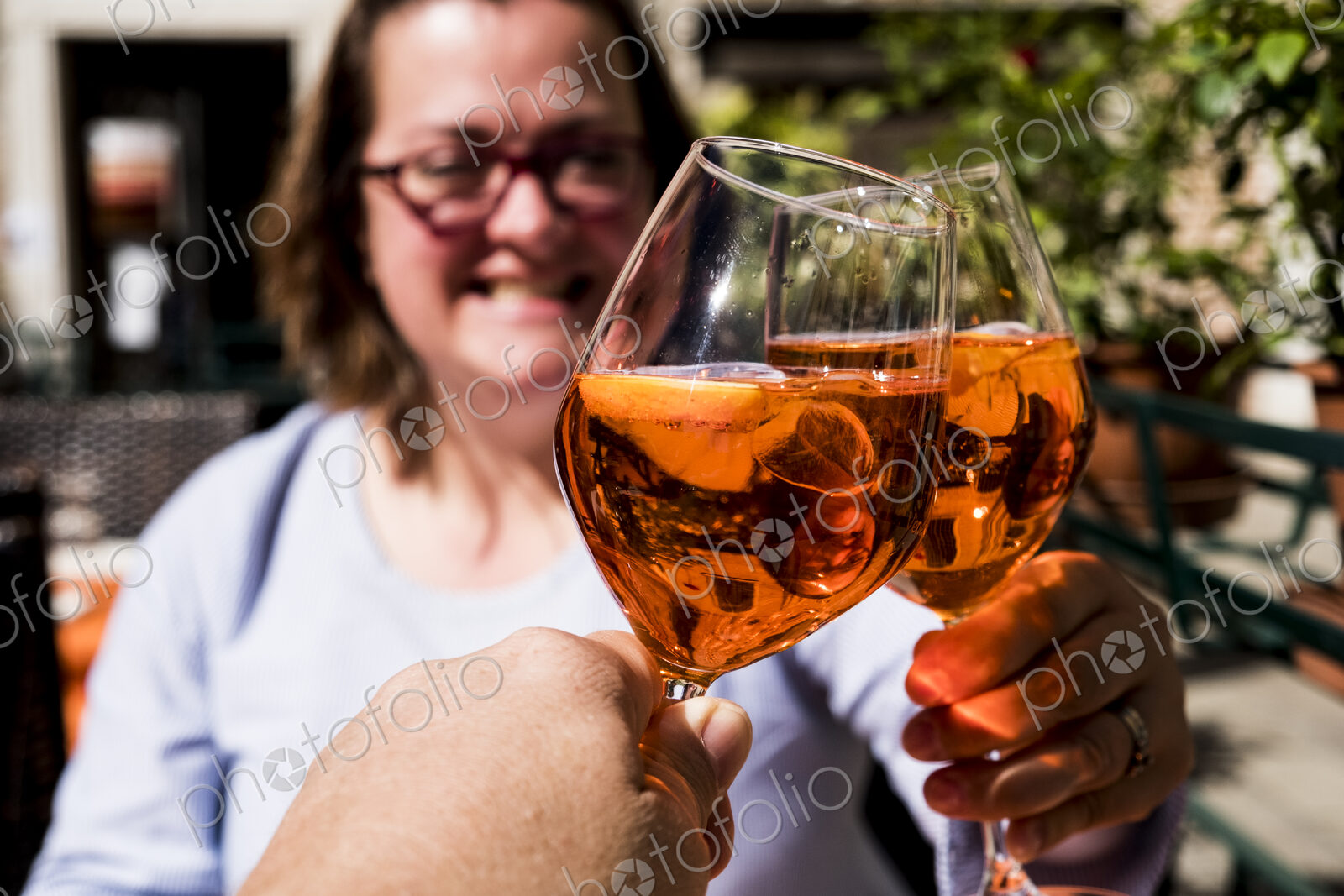 Woman and another person sitting at a table toasting with wine glasses of Aperol Spritz.