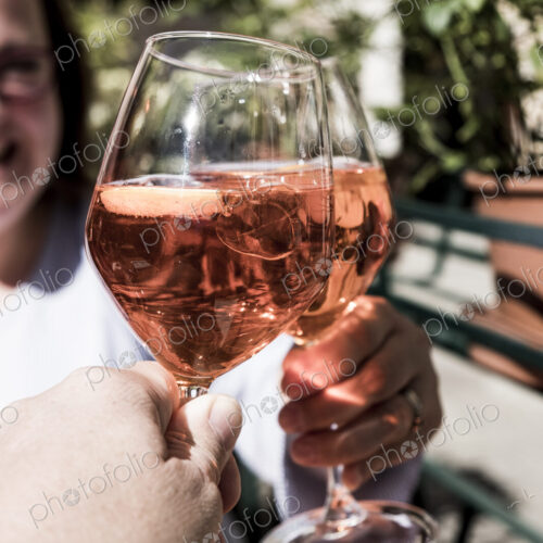 Woman and another person sitting at a table toasting with wine glasses of Aperol Spritz.