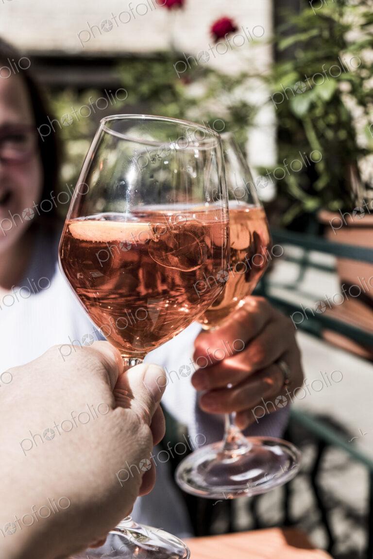 Woman and another person sitting at a table toasting with wine glasses of Aperol Spritz.