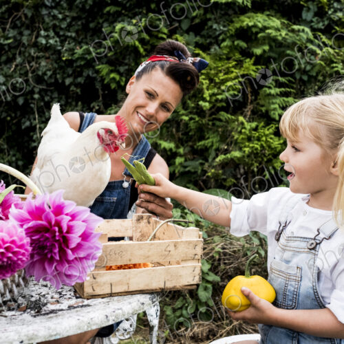 Woman and girl sitting at a table in a garden, feeding white chicken. Woman and girl sitting at a table in a garden, feeding white chicken.