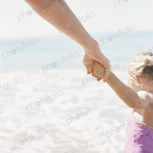 Woman and her daughter holding hands, standing on a sandy beach by he ocean. Woman and her daughter holding hands, standing on a sandy beach by he ocean.