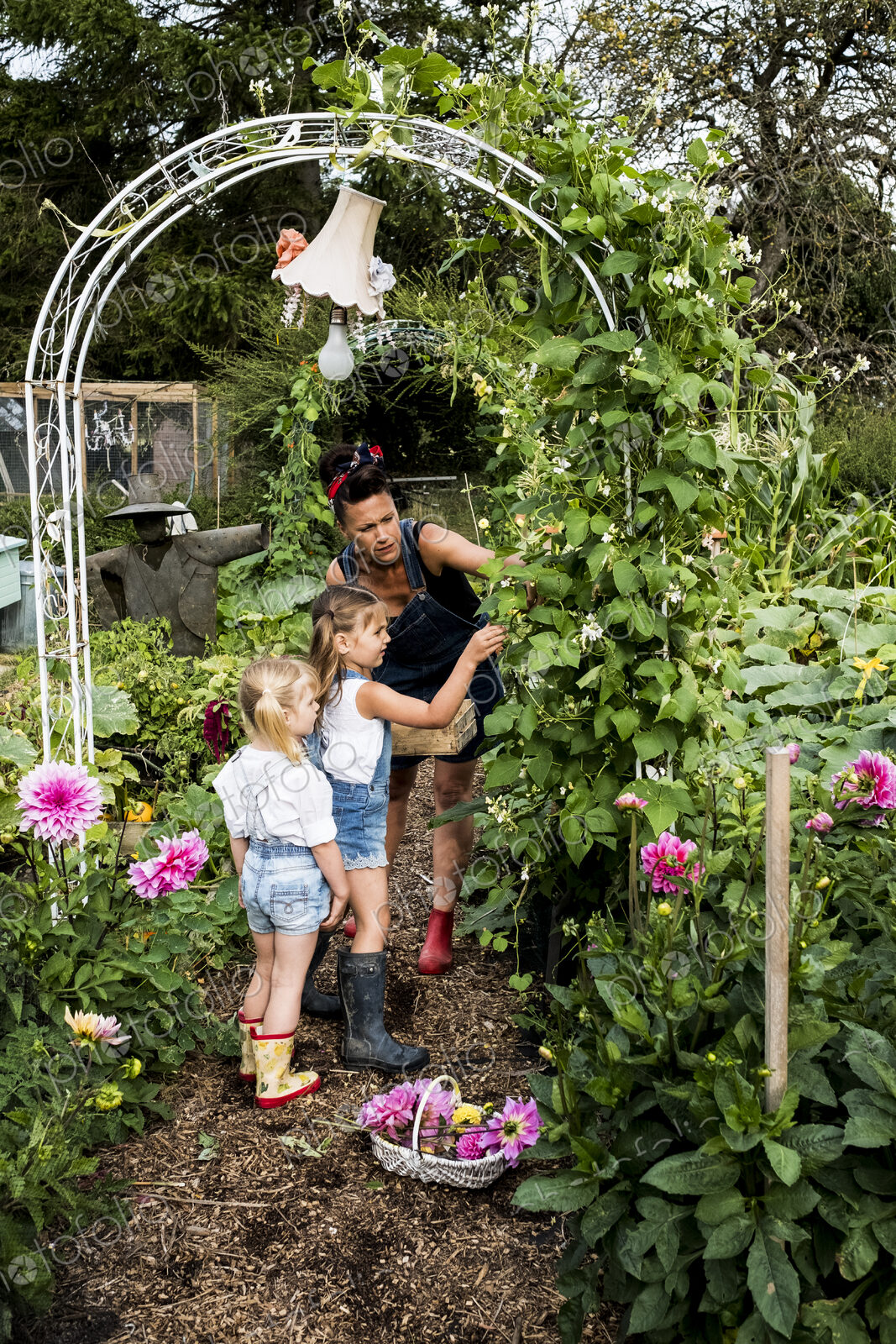 Woman and two girls standing underneath arch in a garden, picking green beans.