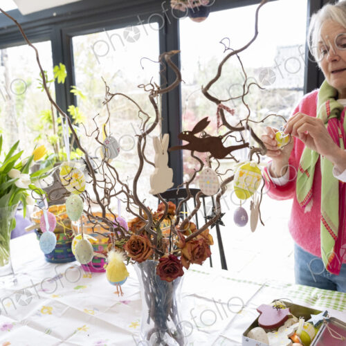 Woman arranging Easter ornaments in vase on kitchen table.