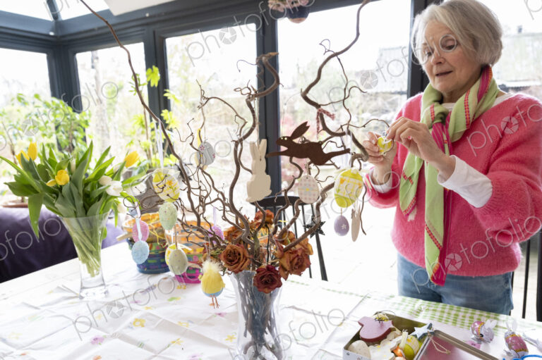 Woman arranging Easter ornaments in vase on kitchen table.