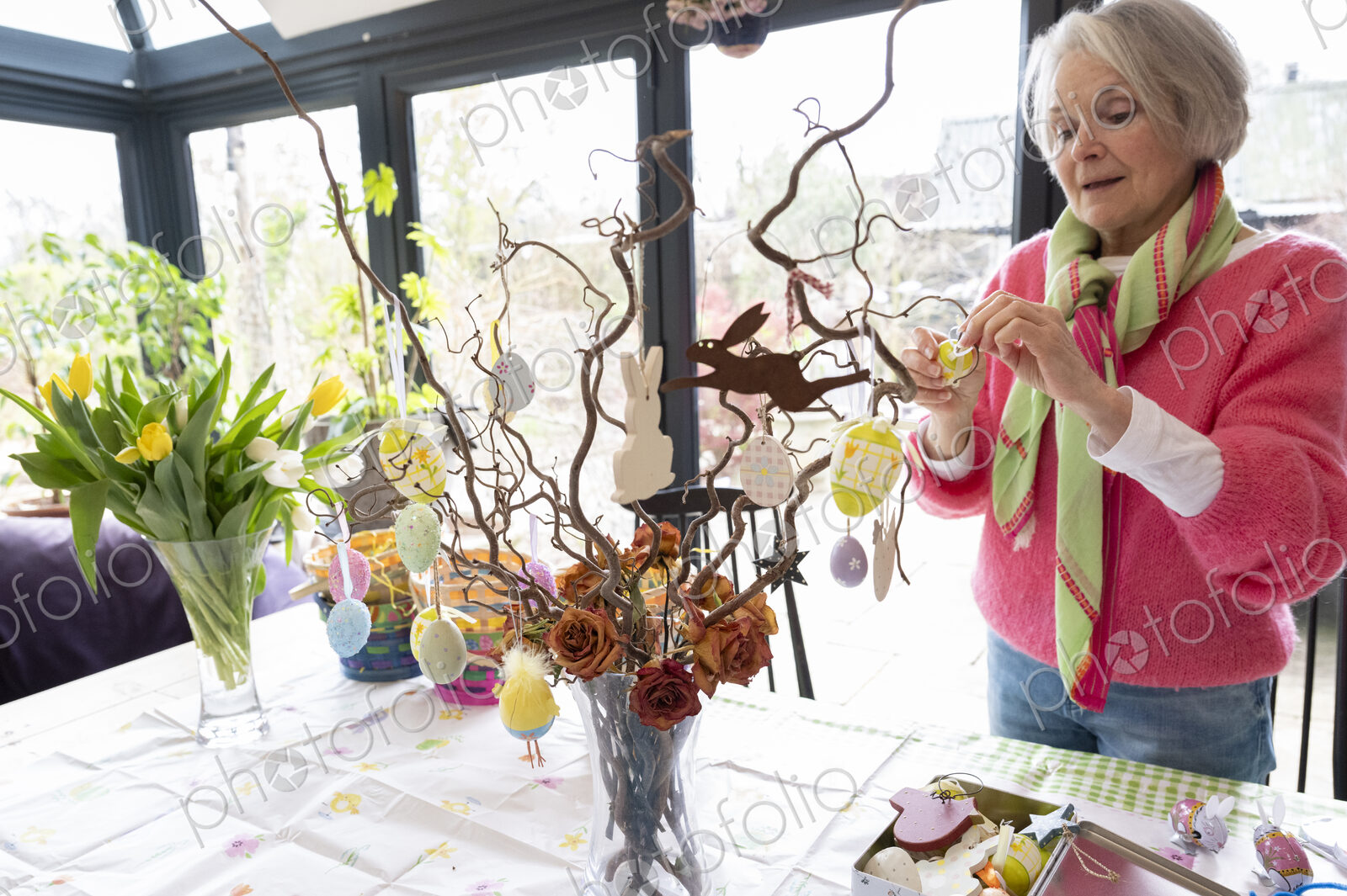 Woman arranging Easter ornaments in vase on kitchen table.