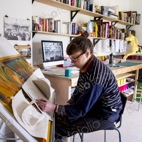 Woman artist sitting at a tilted drawing table in her studio, drawing Woman artist sitting at a tilted drawing table in her studio, drawing
