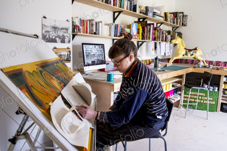 Woman artist sitting at a tilted drawing table in her studio, drawing