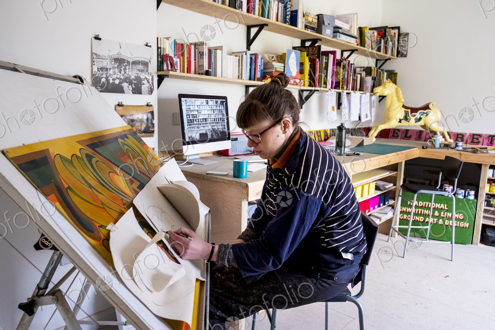Woman artist sitting at a tilted drawing table in her studio, drawing