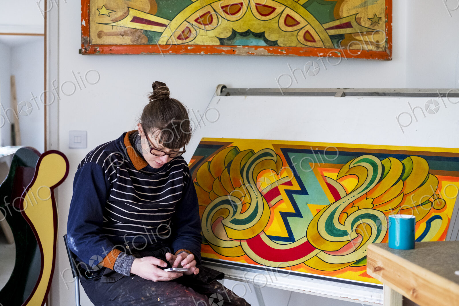 Woman artist sitting by a drawing table checking her mobile phone.