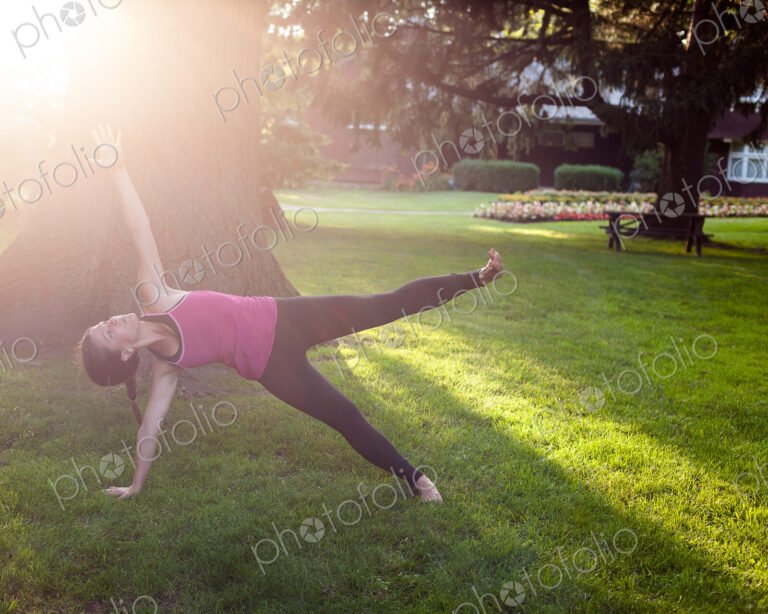 Woman balancing on side in yoga pose in park.