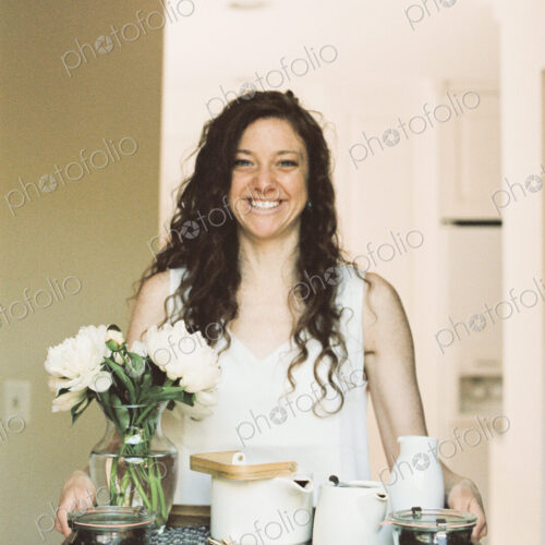 Woman carrying a tray with a teapot and a vase of white roses.