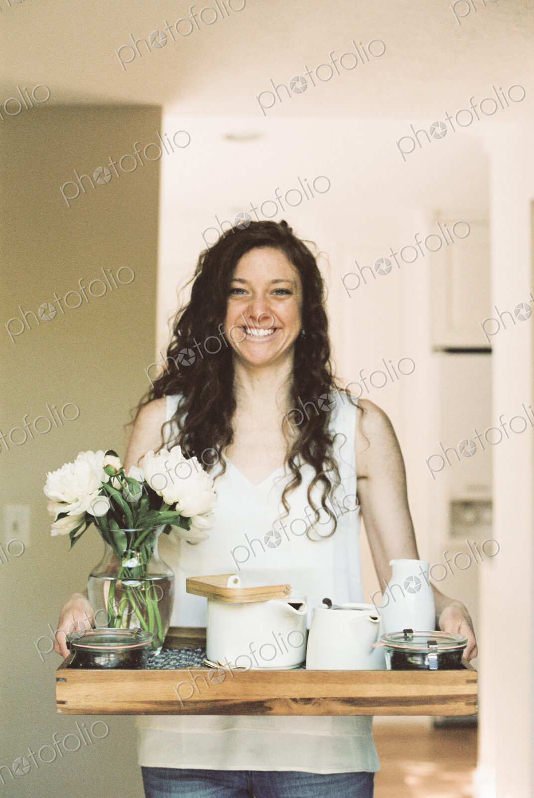 Woman carrying a tray with a teapot and a vase of white roses.