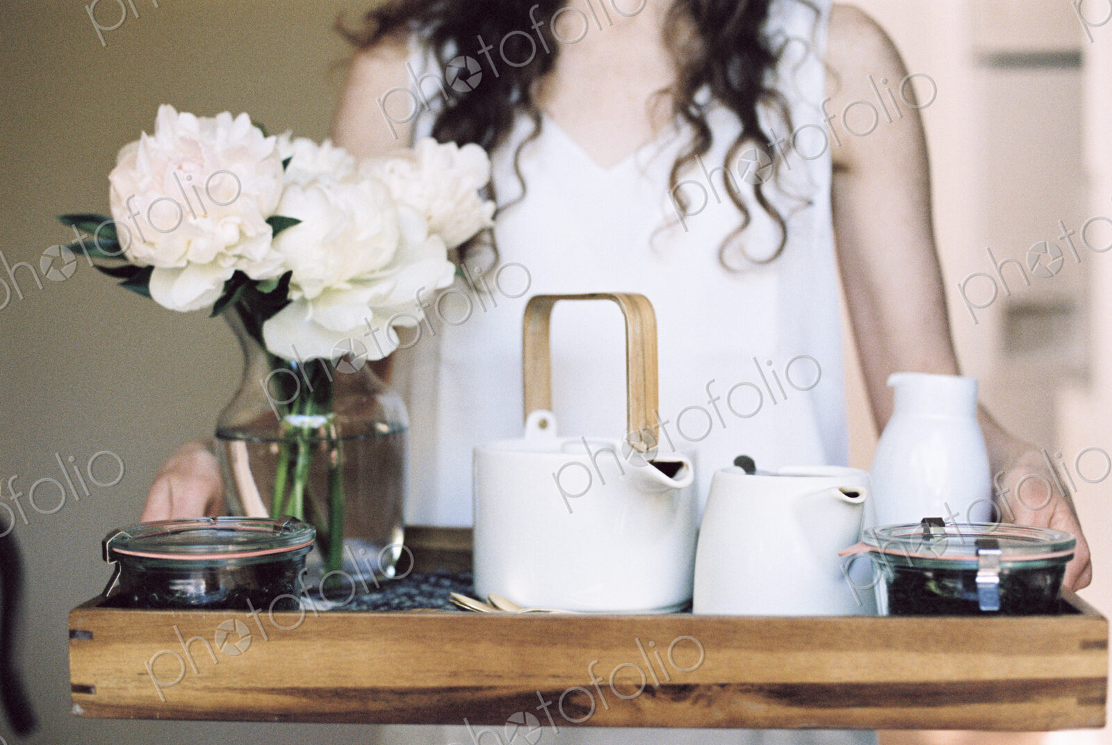 Woman carrying a tray with a teapot and a vase of white roses.