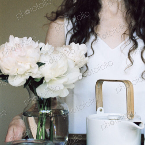 Woman carrying a tray with a teapot and a vase of white roses.