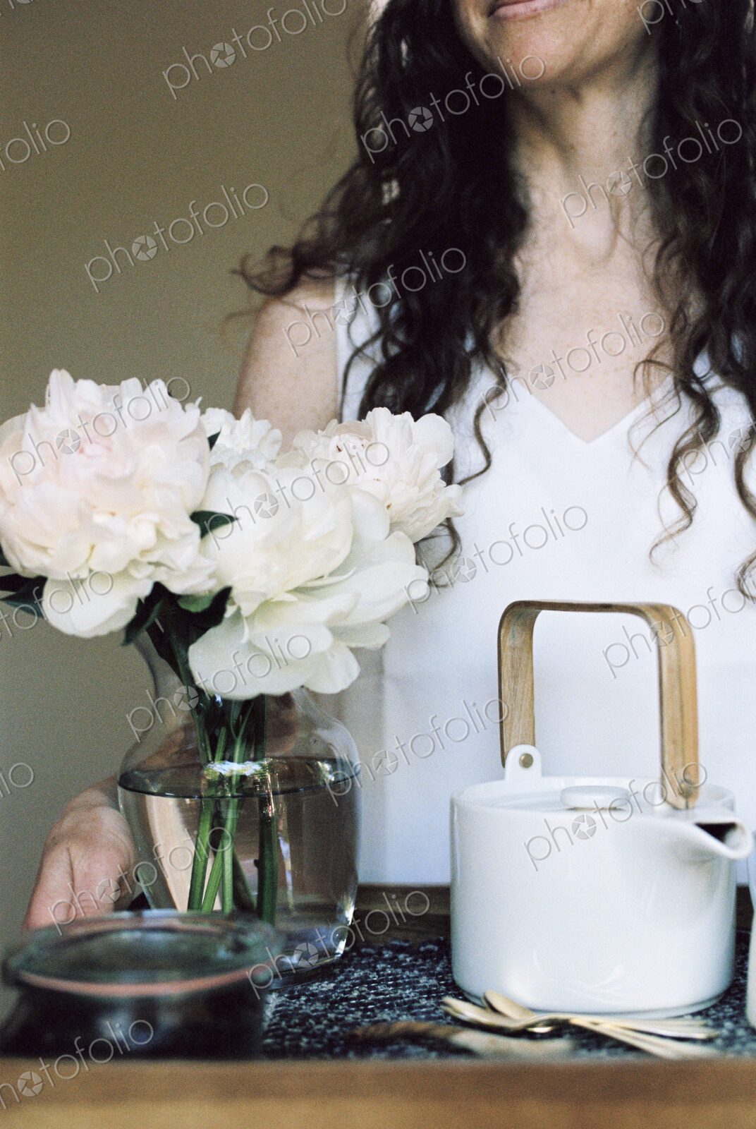 Woman carrying a tray with a teapot and a vase of white roses.