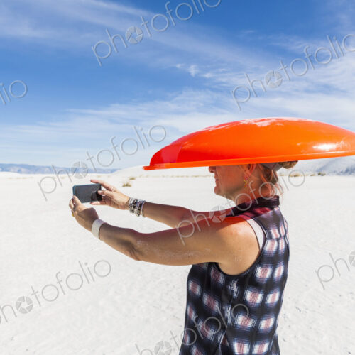 Woman carrying orange sled on her head,taking selfie,White Sands Nat'l Monument, NM