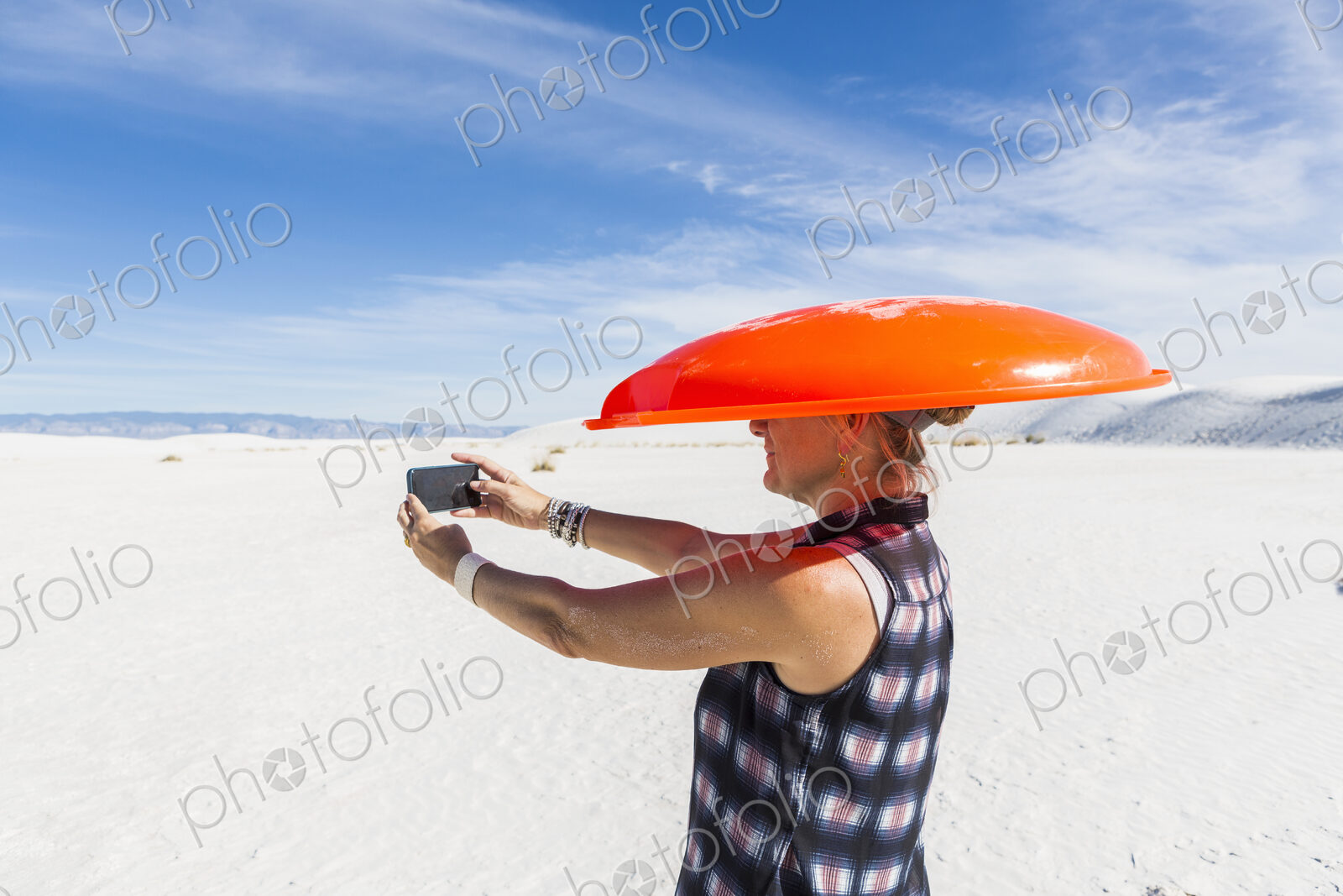 Woman carrying orange sled on her head,taking selfie,White Sands Nat’l Monument, NM