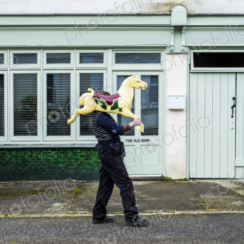 Woman carrying traditional wooden horse from merry-go-round on her shoulder. Woman carrying traditional wooden horse from merry-go-round on her shoulder.