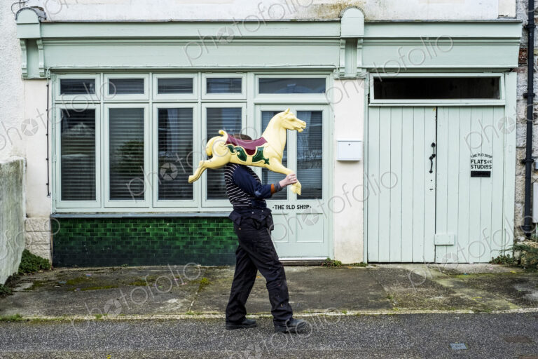 Woman carrying traditional wooden horse from merry-go-round on her shoulder.