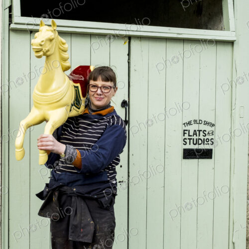 Woman carrying wooden painted carousel galloper horse on her shoulder Woman carrying wooden painted carousel galloper horse on her shoulder