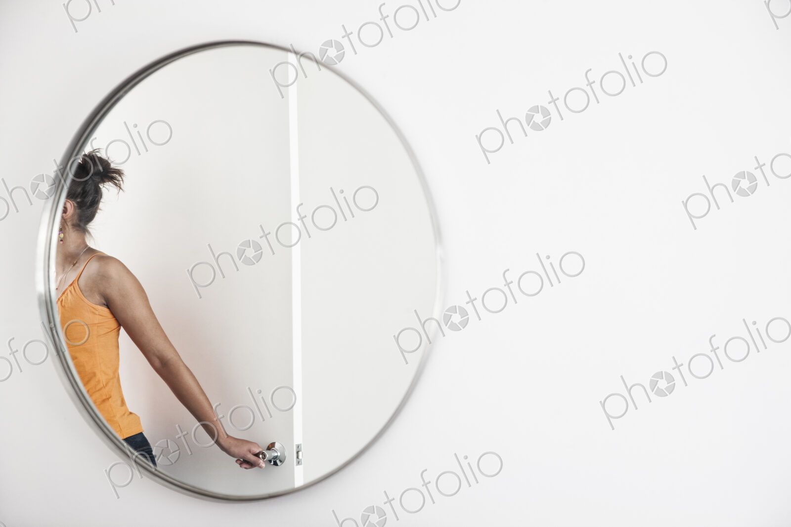 Woman closing a door in a room, reflected in a round mirror.