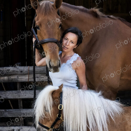 Woman holding a brown bay horse and a small Shetland pony by their reins. Woman holding a brown bay horse and a small Shetland pony by their reins.