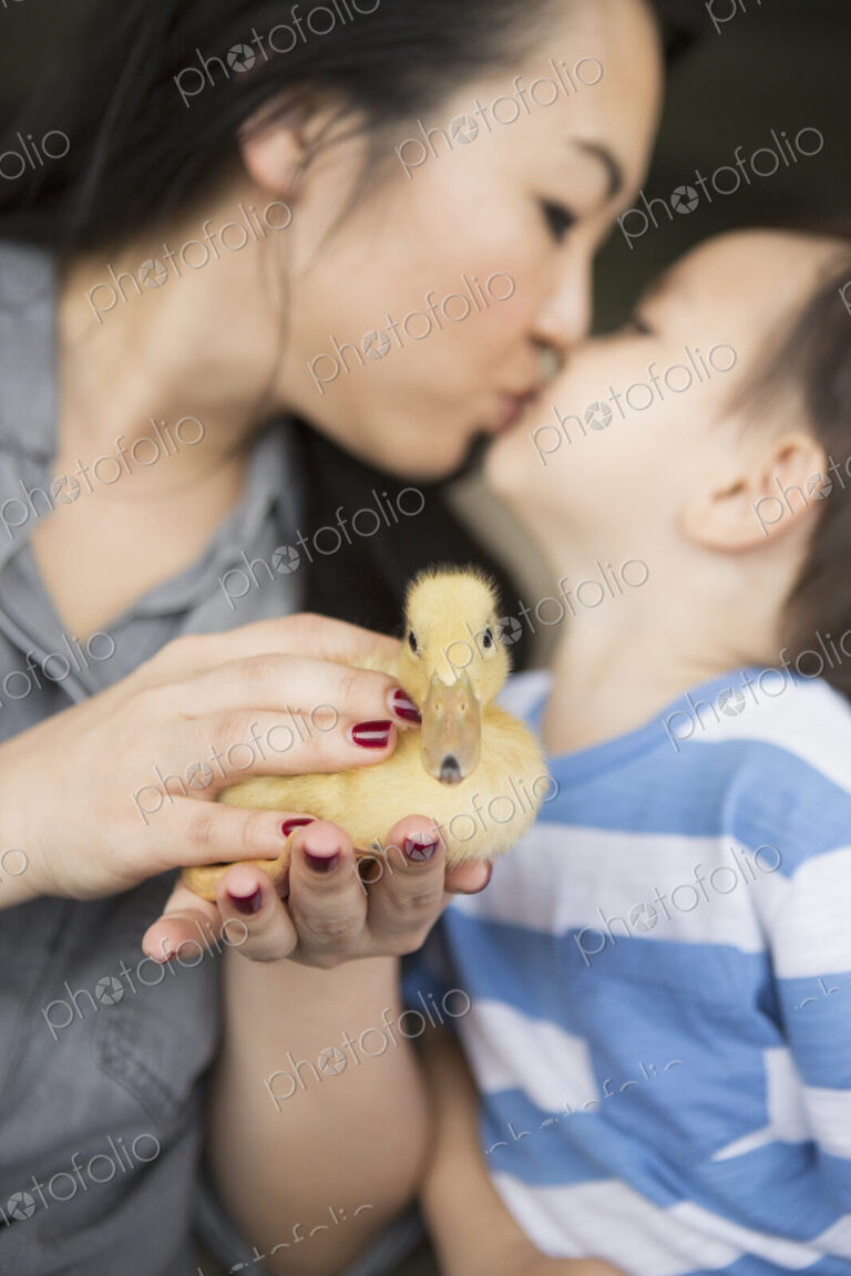 Woman holding a yellow duckling in her hands, kissing her young son.