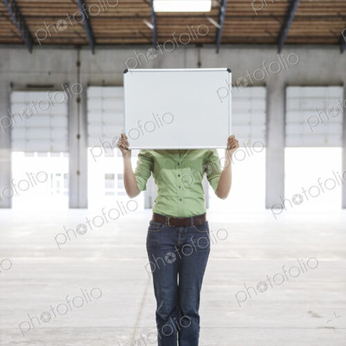 Woman holding up a blank slate in an empty warehouse space. Woman holding up a blank slate in an empty warehouse space.