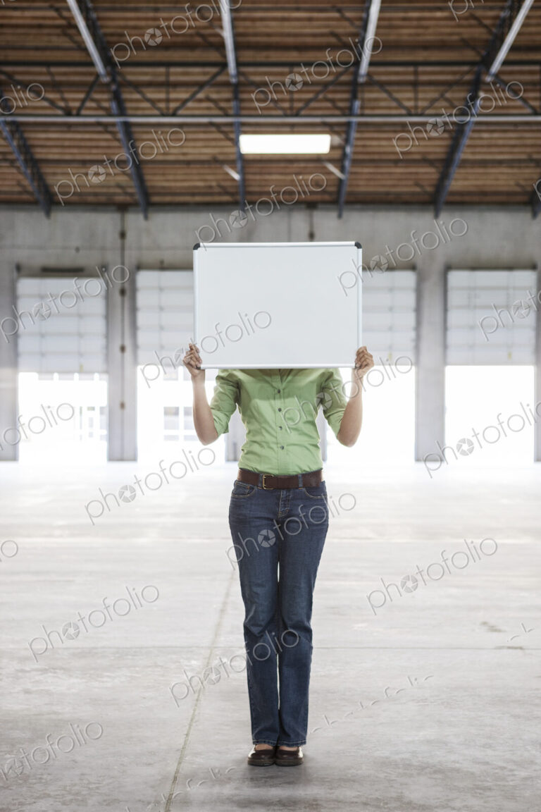 Woman holding up a blank slate in an empty warehouse space.