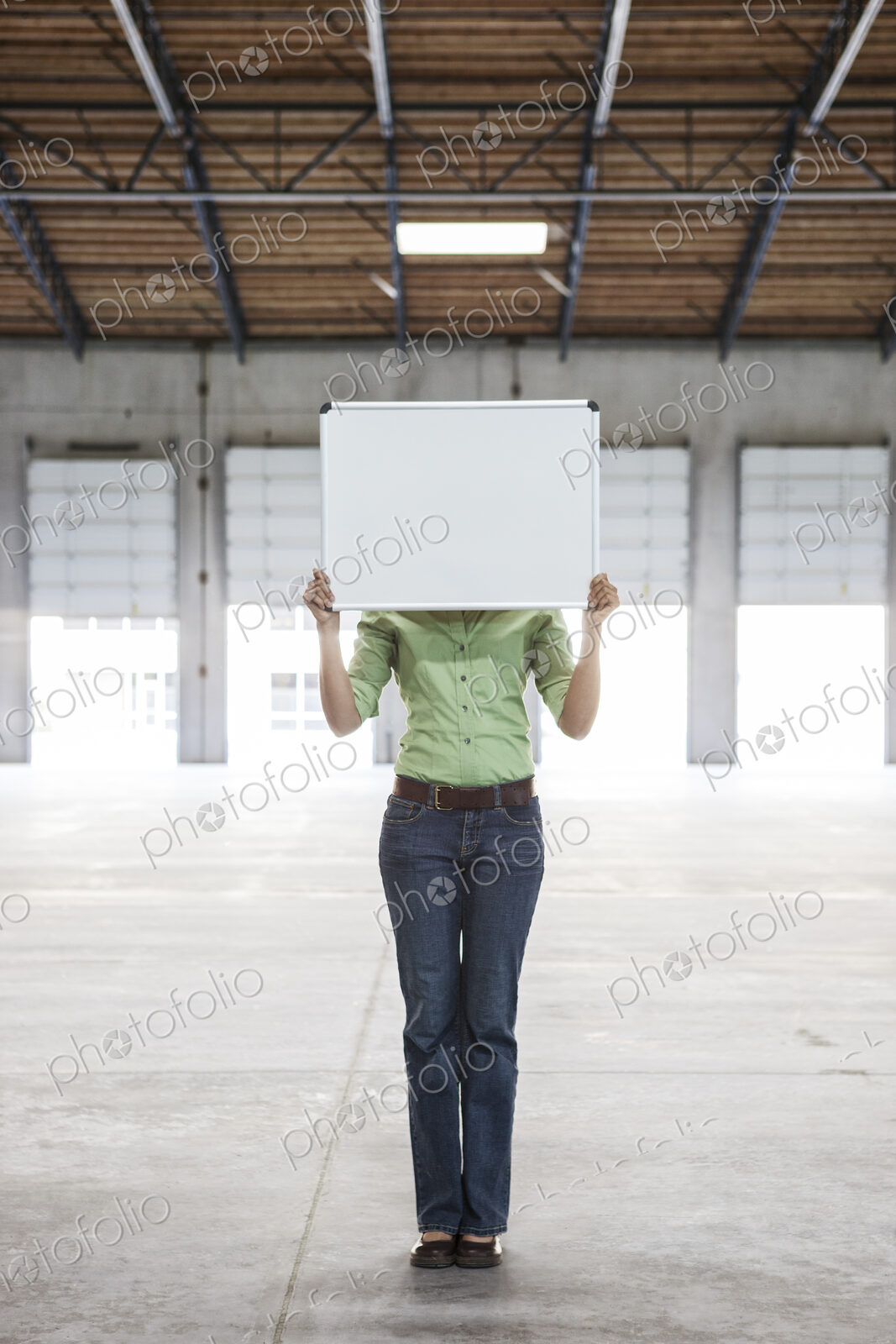 Woman holding up a blank slate in an empty warehouse space.