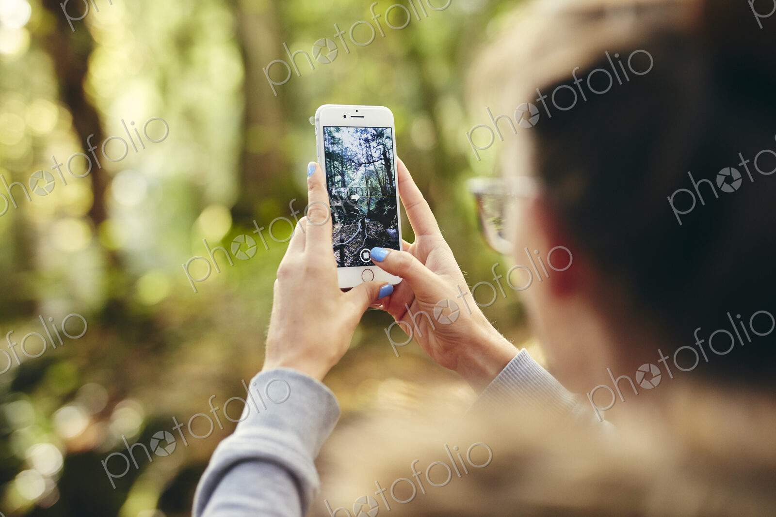 Woman holding up mobile phone outdoors in woodland.