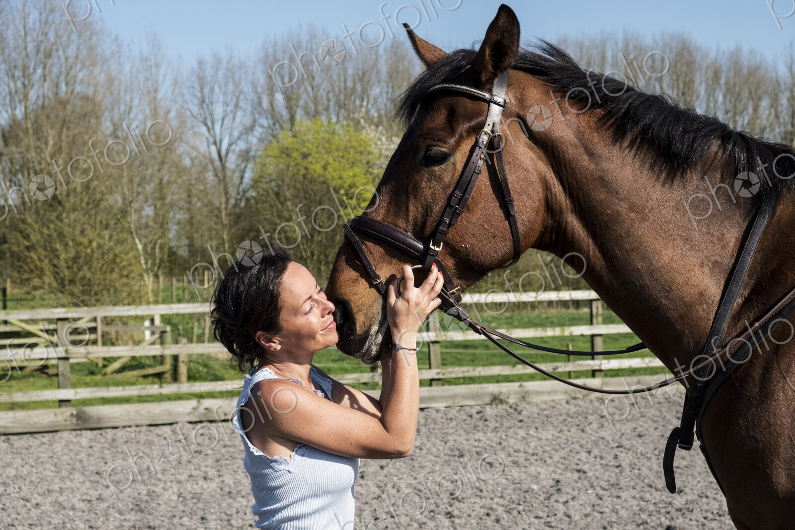 Woman horse trainer standing in a paddock, holding a bay brown horse by the bridle