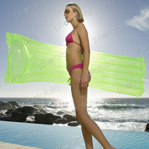 Woman in a bikini on a beach carrying inflatable lilo.