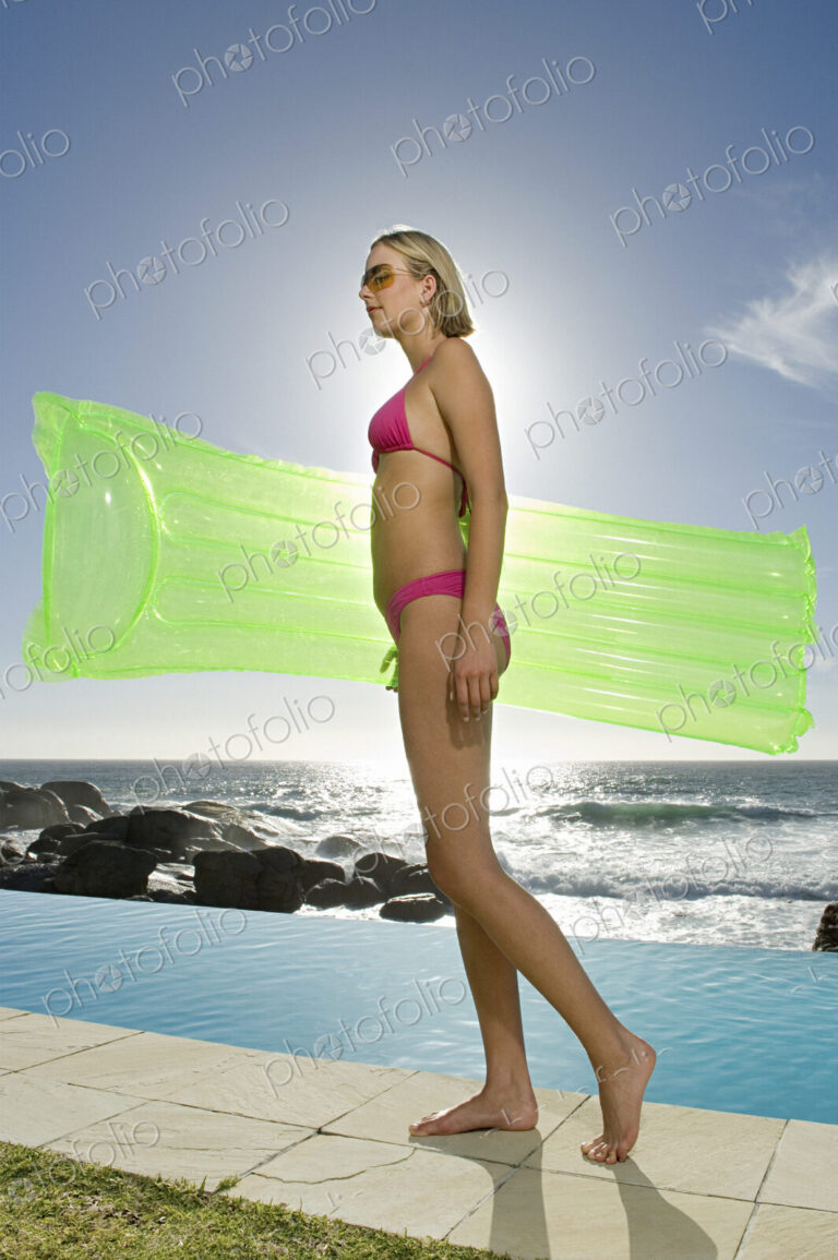 Woman in a bikini on a beach carrying inflatable lilo.