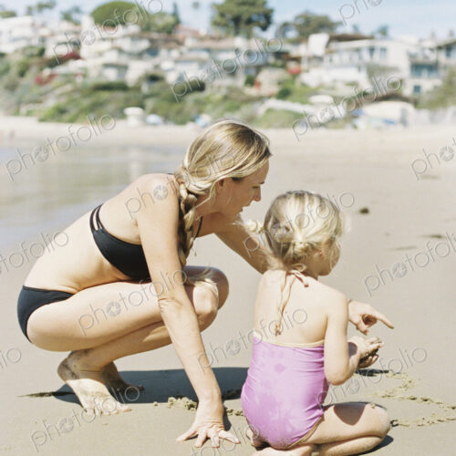 Woman in a bikini playing with her daughter on a sandy beach.