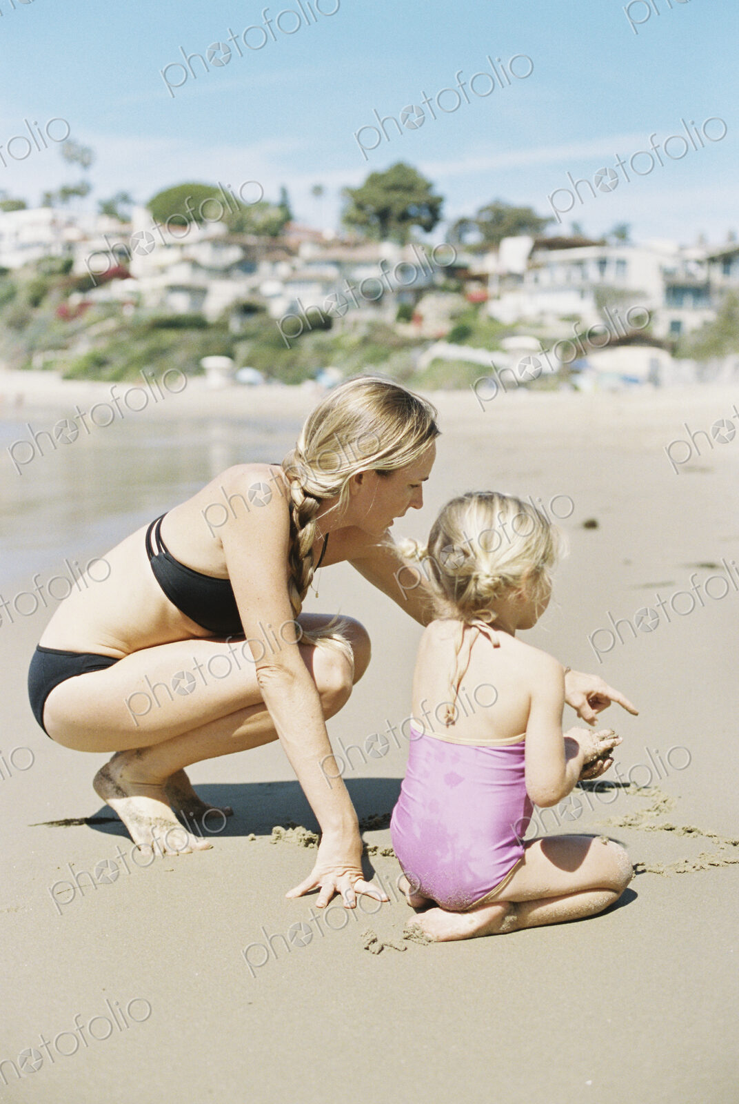 Woman in a bikini playing with her daughter on a sandy beach.