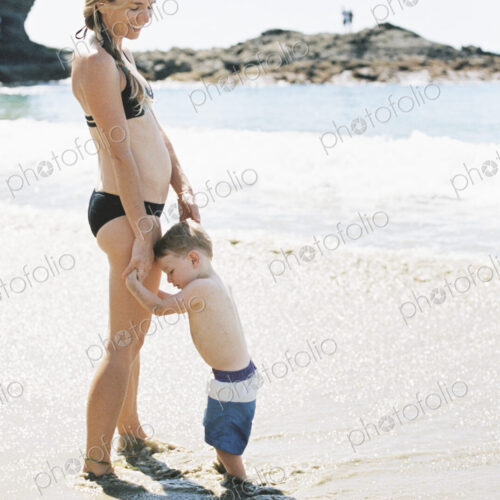 Woman in a bikini playing with her son on a sandy beach by the ocean.