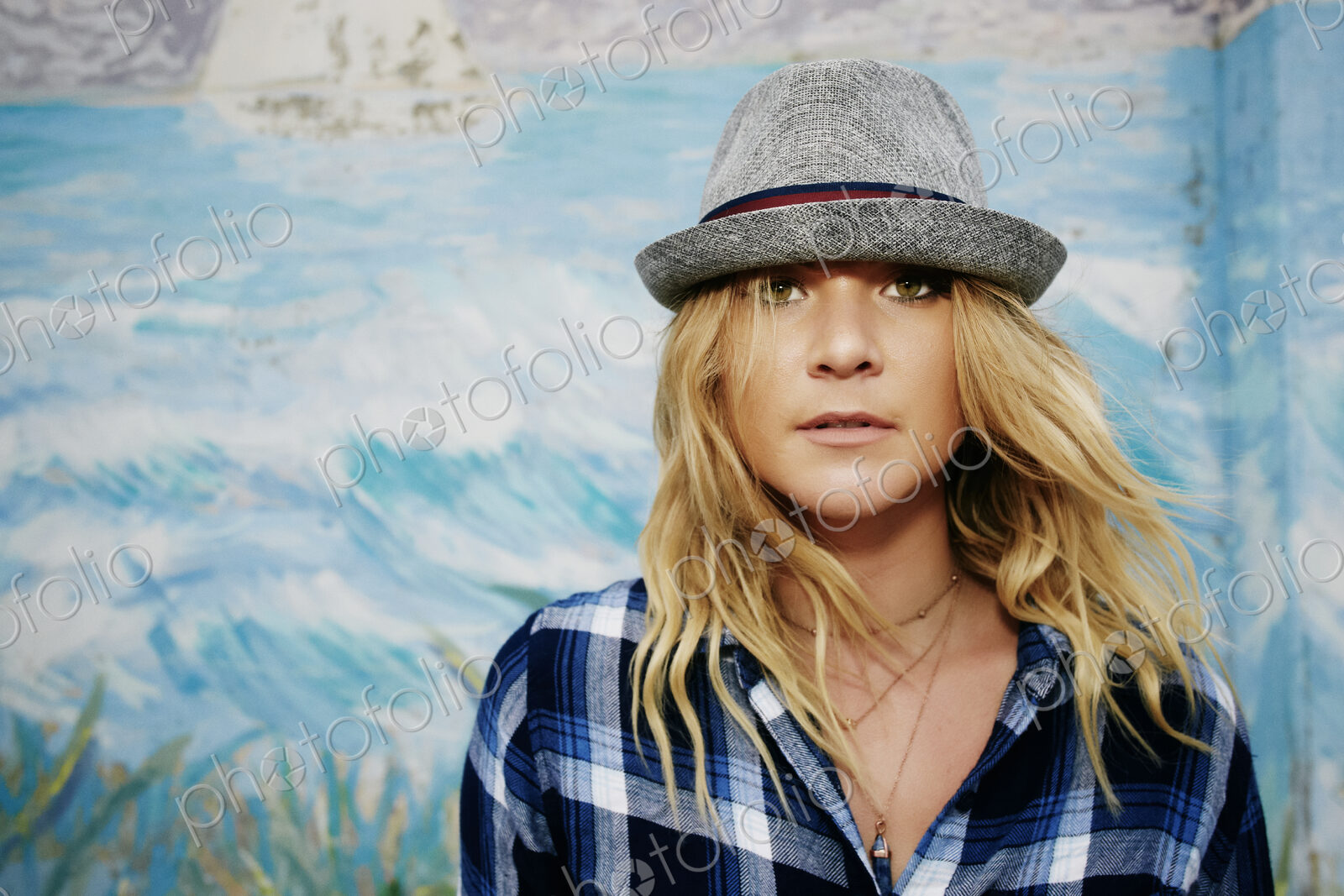 Woman in a blue checkered shirt and grey Trilby hat, looking at camera.