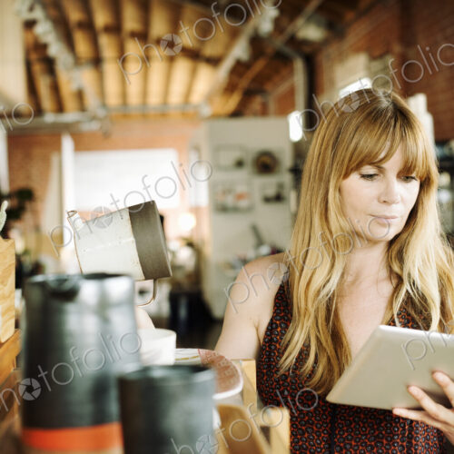 Woman in a shop, holding a digital tablet and ceramic jug.
