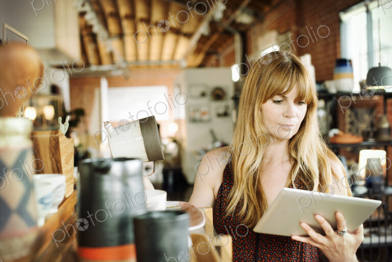 Woman in a shop, holding a digital tablet and ceramic jug.