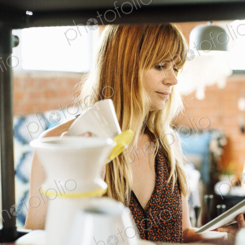 Woman in a shop, holding a digital tablet and small ceramic pot. Woman in a shop, holding a digital tablet and small ceramic pot.