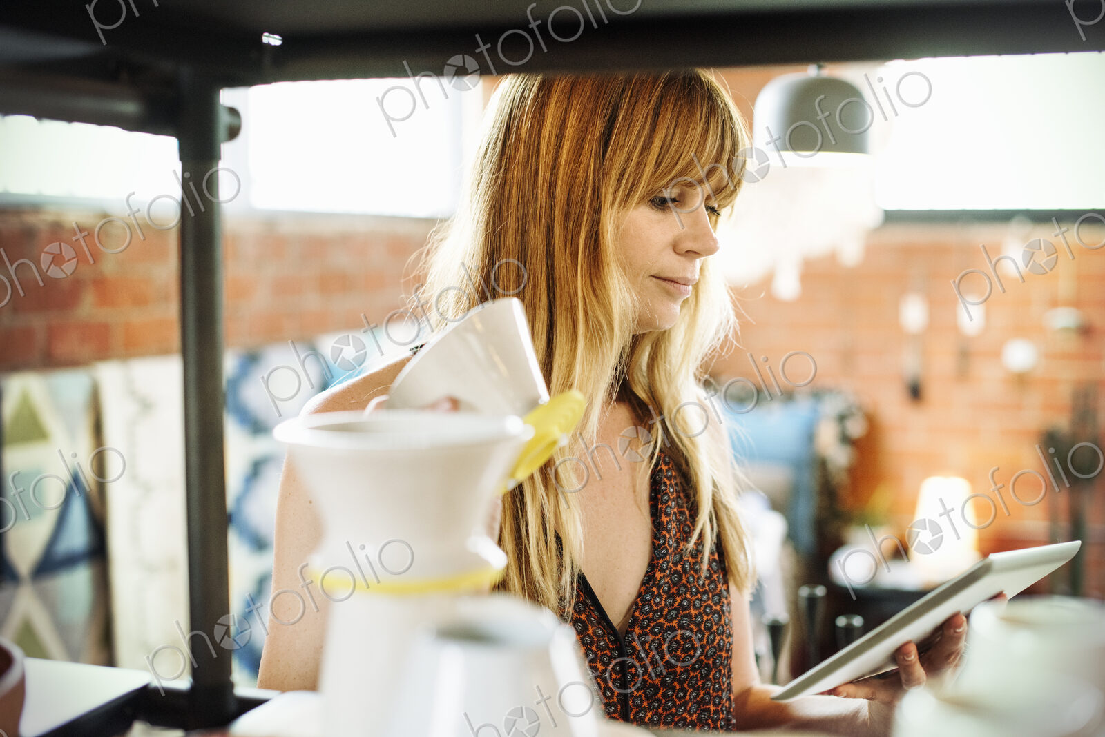 Woman in a shop, holding a digital tablet and small ceramic pot.