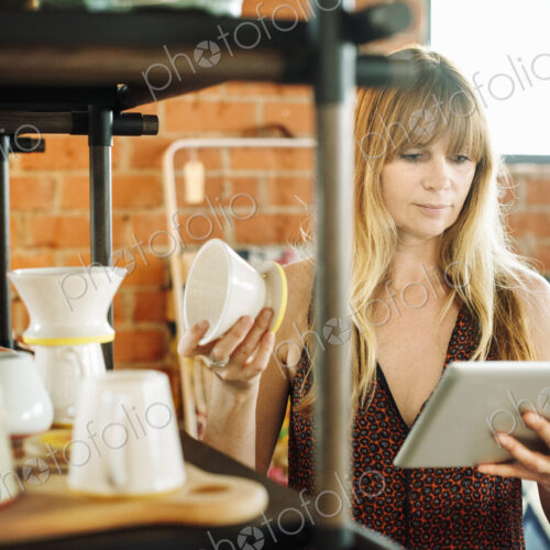 Woman in a shop, holding a digital tablet and small ceramic pot.