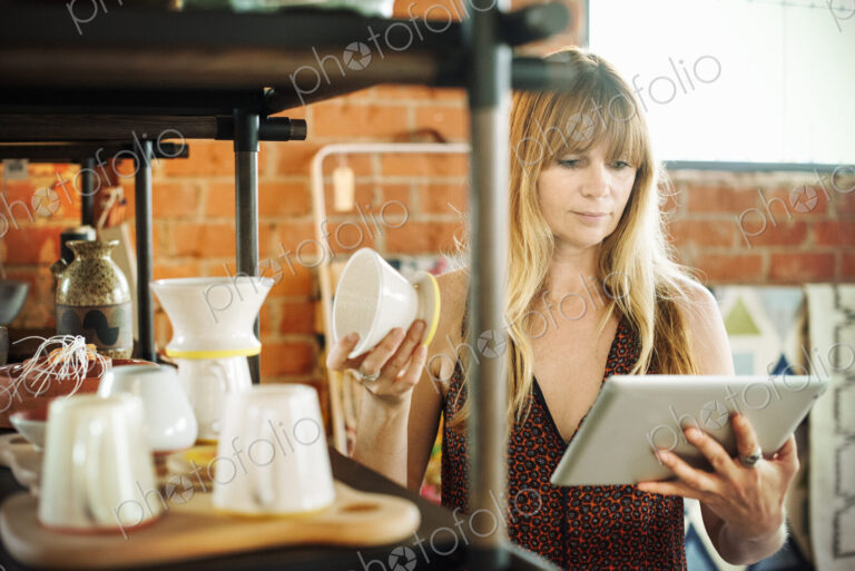 Woman in a shop, holding a digital tablet and small ceramic pot.