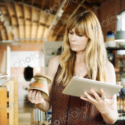 Woman in a shop, holding a digital tablet and small ceramic pot.