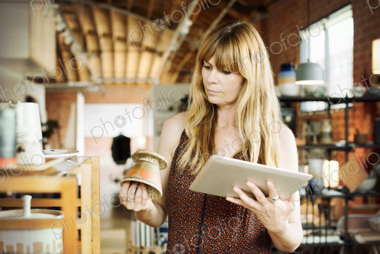 Woman in a shop, holding a digital tablet and small ceramic pot.