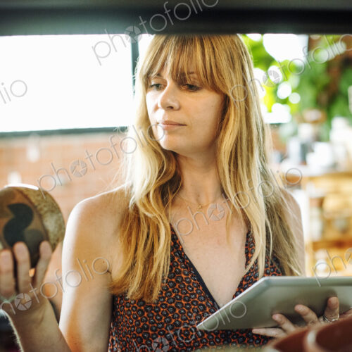 Woman in a shop, holding a digital tablet and small ceramic vase.